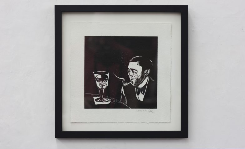 framed linocut print titled drinks. Print depicts a man smoking a pipe and talking to his cocktail glass drink